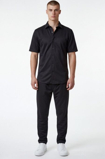 Full-body shot of a man in an all-black outfit: short-sleeve button-down shirt and matching pants with white sneakers.