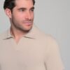 Man with dark hair and stubble wearing a light beige polo shirt, looking off to the left.