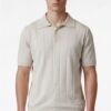 Male model wearing a beige ribbed short-sleeve polo shirt standing against a white background.
