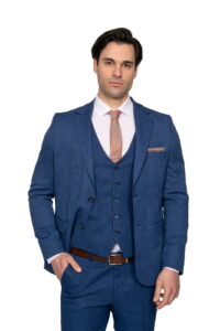 IMG_4749 - Noble Man in a blue three‑piece suit (jacket, vest, trousers) with white shirt and peach tie, standing with one hand in pocket.