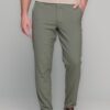 Man wearing a beige top and olive green pants with brown leather shoes, standing with one hand in his pocket.