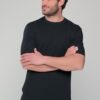 Man with dark hair and stubble wearing a black short-sleeve shirt, arms crossed, facing left.