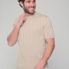 Smiling man with dark hair wearing a beige ribbed short-sleeve sweater and white pants, posing against a light gray background.