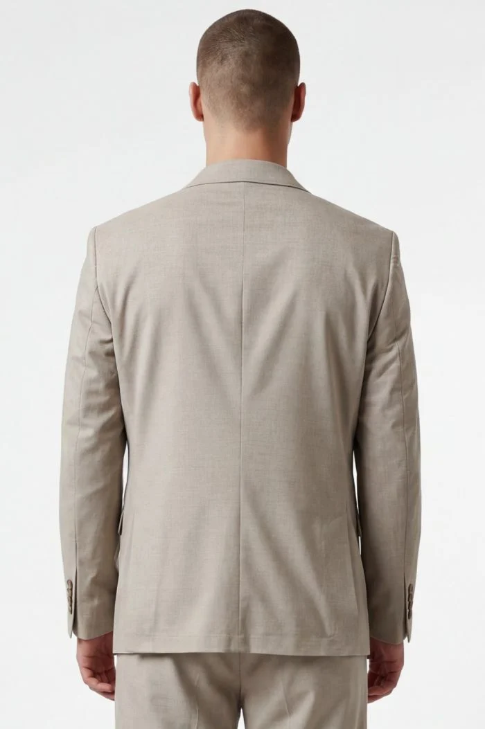 Back view of a person wearing a light beige suit jacket and matching trousers, standing against a neutral background
