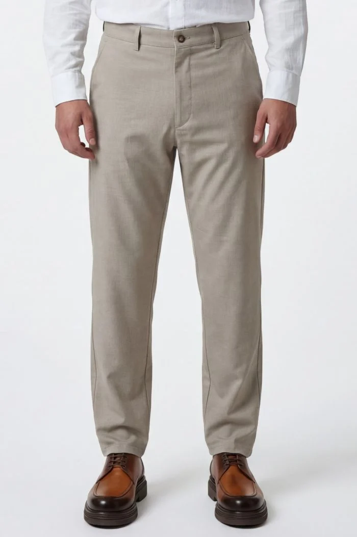 Man wearing beige chinos with a white dress shirt and brown dress shoes, full-length view.