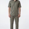 Male model wearing an olive-green short-sleeve button-down shirt with matching olive pants and white sneakers.