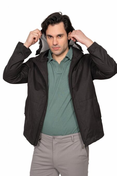 Man wearing a black jacket and green polo shirt pulls the hood up, against a white background.