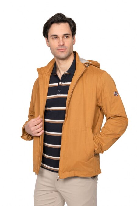 Man wearing a tan zippered jacket over a navy striped polo, standing against a white background.