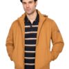 Man wearing a mustard-colored jacket over a navy striped polo, standing against a white studio background.