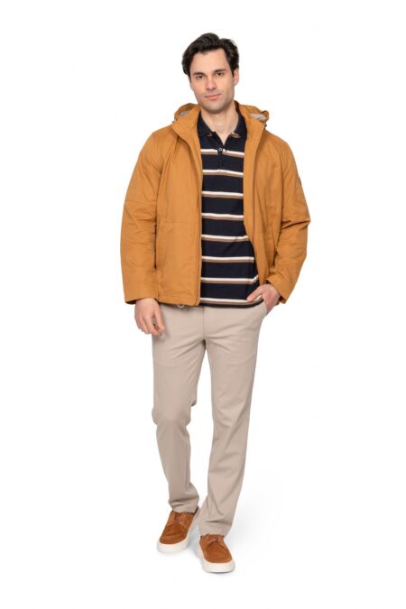 Man modeling a camel-colored jacket over a navy striped polo, beige chinos, and brown sneakers, standing with a hand in his pocket.