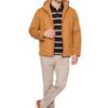 Man posing in a camel-colored jacket over a navy striped polo, beige pants, and brown sneakers.