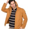 Man modeling a tan hooded jacket over a navy striped polo, with one hand in his hair looking down.