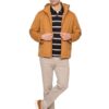 Man posing in a tan jacket over a navy striped polo with beige pants and brown suede sneakers, hands adjusting the zipper.