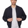 Man wearing a navy bomber jacket over a light grey polo, standing against a white background and holding the zipper.