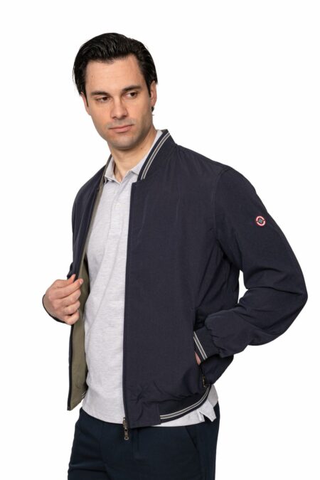 Man wearing a navy bomber jacket over a light gray polo, looking to his left with hand at the jacket. Or alternative: A man in a navy jacket peels open the front, gazing to the side.