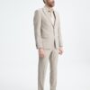 Full-body shot of a man in a light beige suit and black dress shoes, standing and looking to the side in a studio setting.