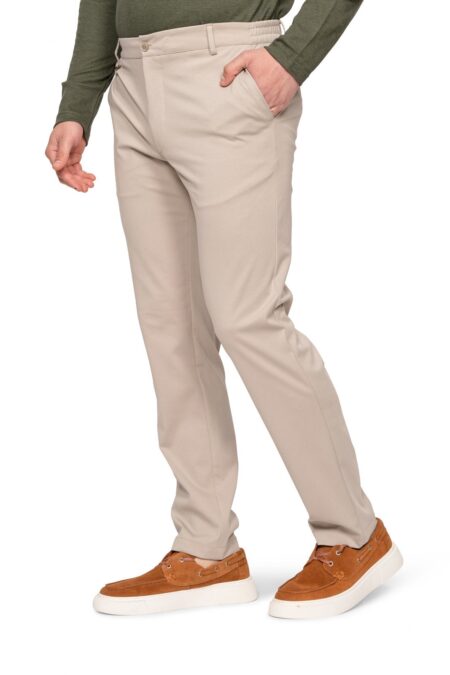 Person wearing beige chinos with hands in pockets, paired with a dark green sweater and brown suede sneakers.