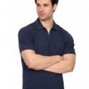 Man with dark hair in a navy polo shirt and beige pants stands with arms crossed against a white background, looking to the side.