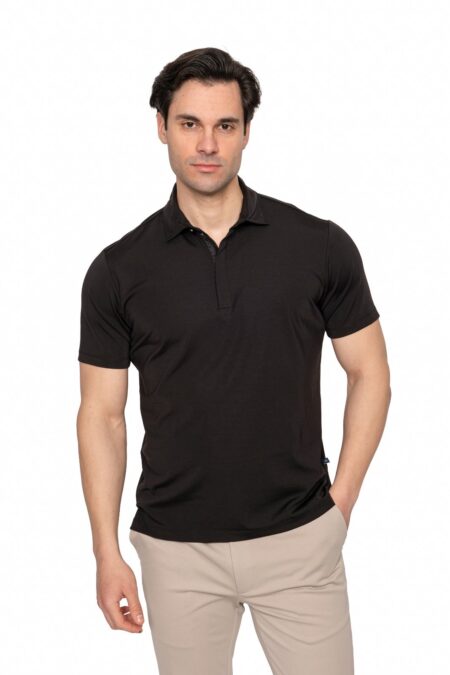 Man wearing a black polo shirt and beige pants, standing against a white studio background.