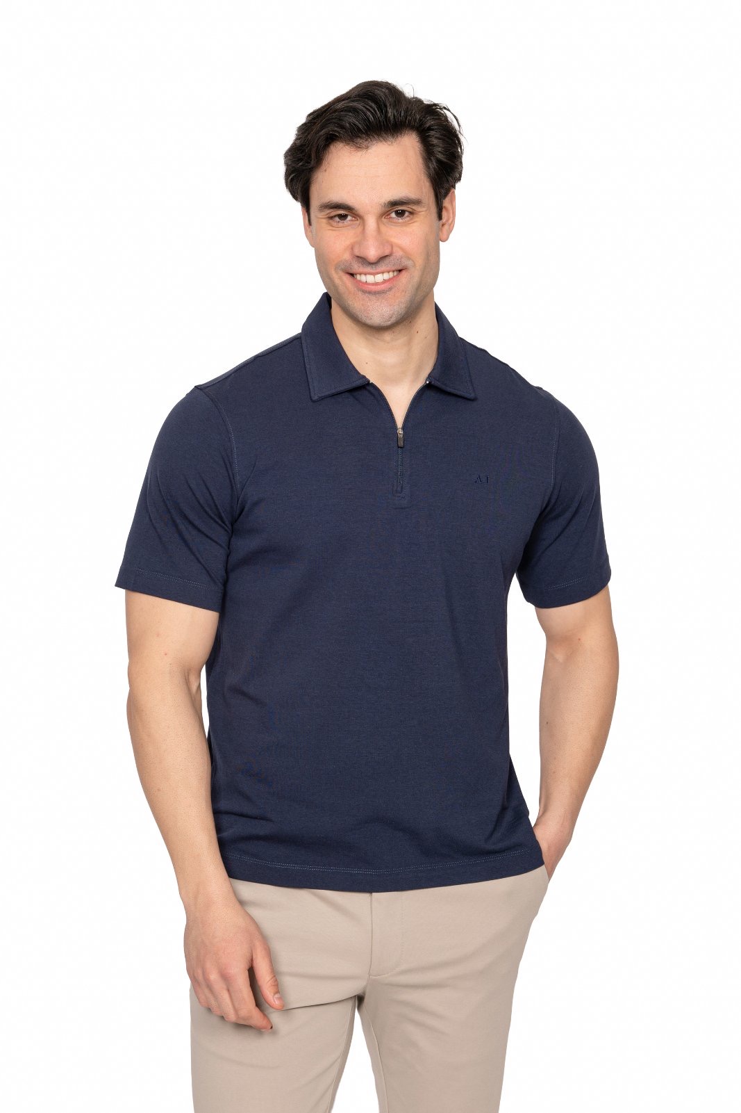 IMG_4966jpg - Noble Smiling man in a navy polo shirt and beige pants standing against a white background, facing the camera.