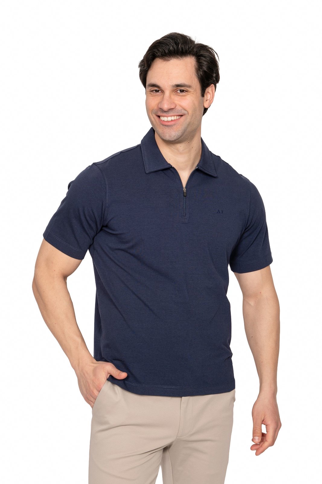 IMG_4973jpg - Noble Smiling man in a navy polo shirt and beige pants poses with one hand in his pocket against a white background.