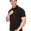 Smiling man in a black polo shirt and beige pants, posing with his right hand on his chest against a white background.