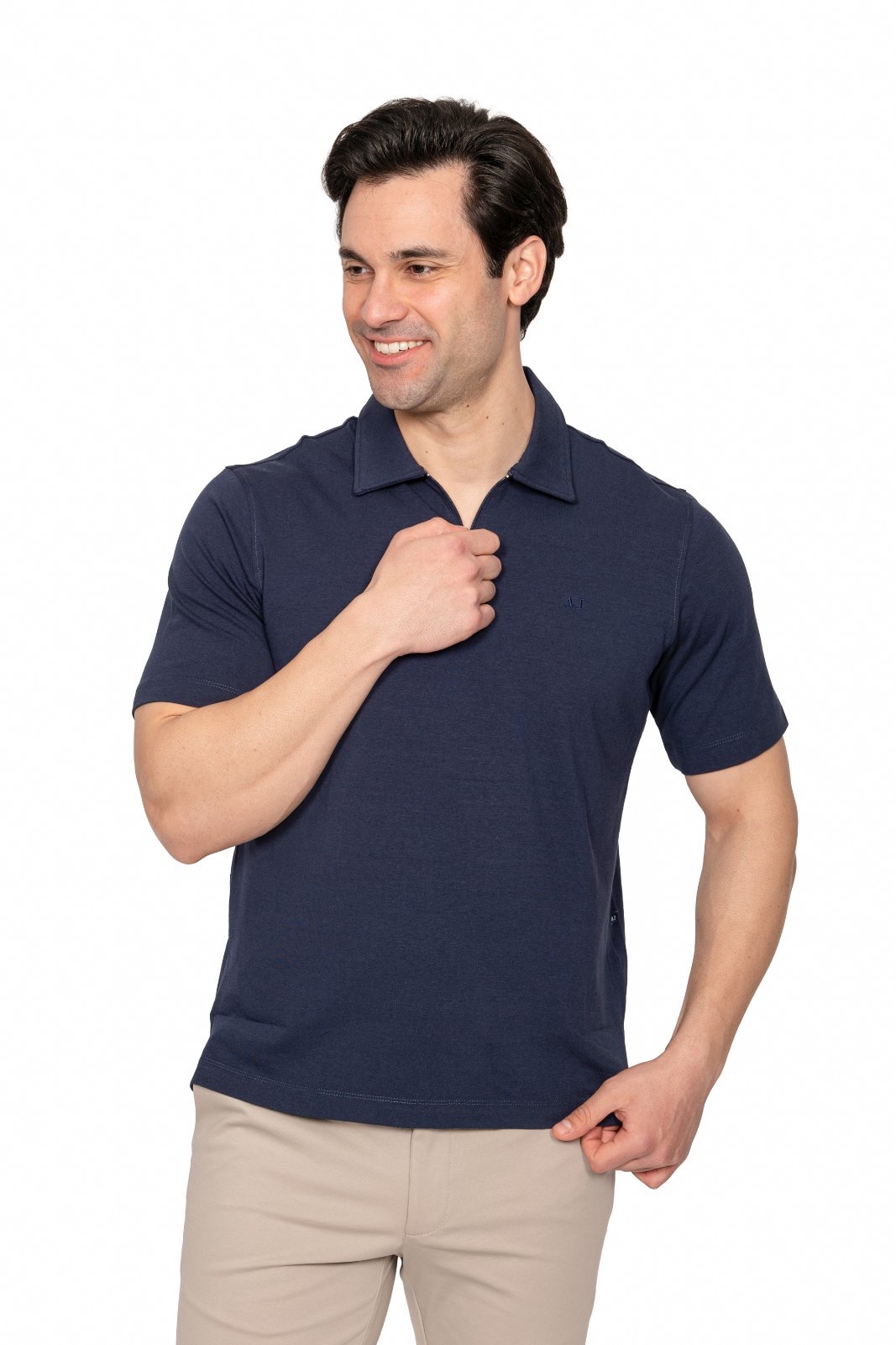 IMG_4991jpg - Noble Man in a navy polo shirt smiles softly while adjusting his collar with his right hand, standing against a white background.