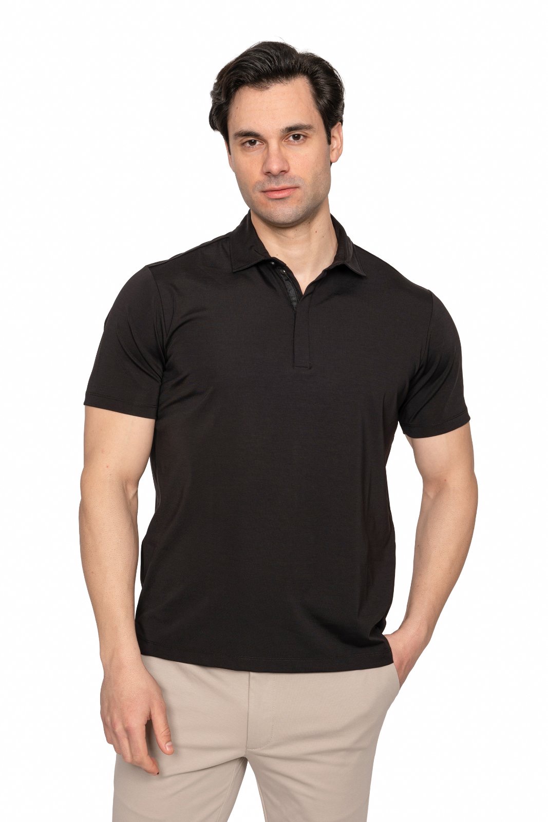 IMG_5041jpg - Noble Man wearing a black polo shirt and beige pants, standing against a white studio backdrop and looking at the camera.