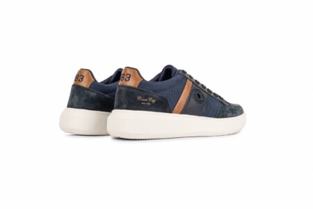 Navy blue sneakers with tan suede accents and a thick white sole, shown from the rear side.