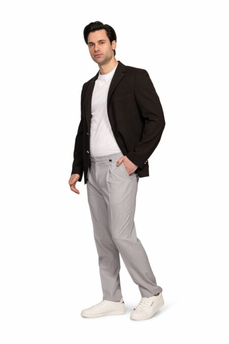 Man in a black blazer, white tee, and light gray trousers poses casually with one hand in pocket, white sneakers.