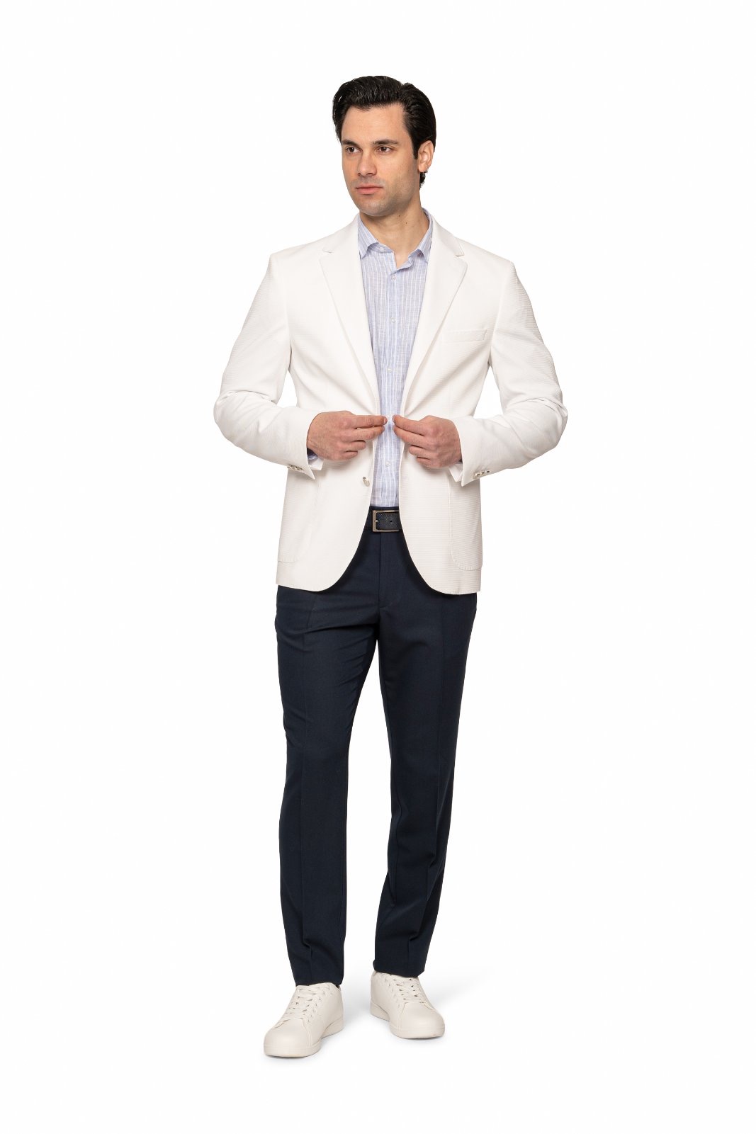 IMG_5142jpg - Noble Man in a white blazer, light striped shirt, navy trousers, and white sneakers posing while buttoning his blazer.