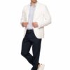 Man in a white blazer, light shirt, navy trousers, and white sneakers posing with hands on his blazer.
