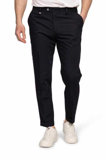 Man wearing navy dress pants with white sneakers, standing with hands at sides.