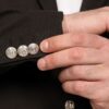 Close-up of a man's cuff with four silver decorative cufflinks on a dark suit sleeve.