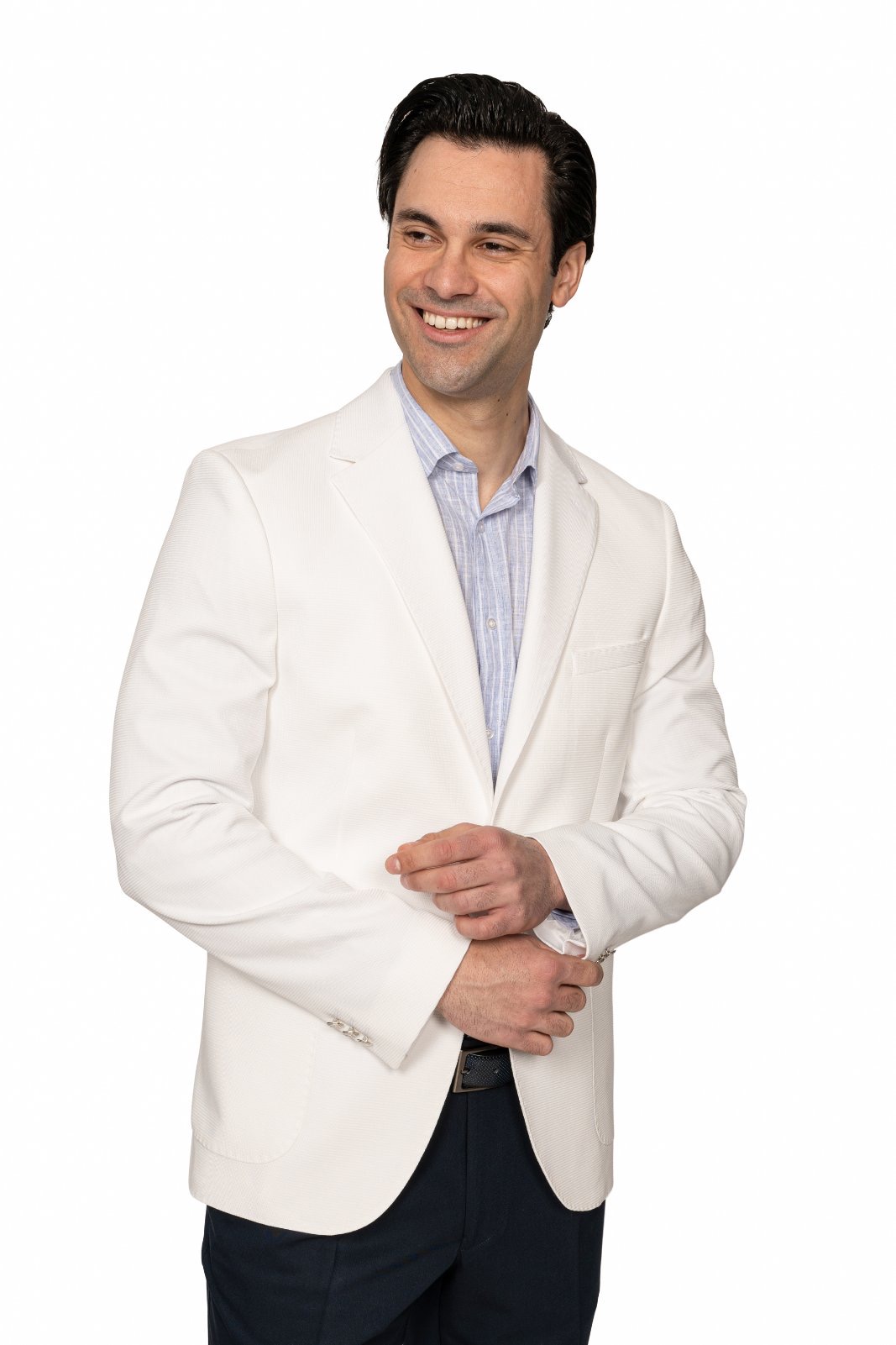 IMG_5218jpg - Noble Smiling man in a light beige blazer and light blue shirt, hands clasped in front against a white background.
