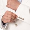 Close-up of a person in a white suit adjusting the cuff with silver decorative cufflinks.