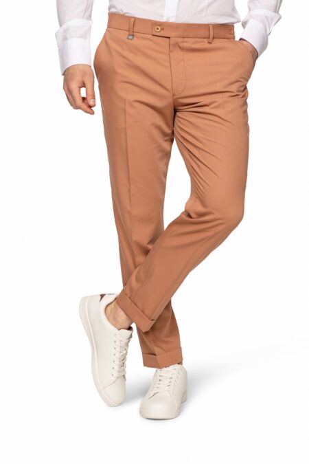 Man wearing tan chinos with a white shirt and white sneakers, standing with one leg crossed.