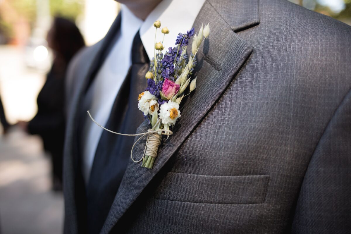 Close-up of a gray checkered suit with a floral boutonniere pinned to the lapel, featuring dried lavender and small white flowers with a pink rose bud.